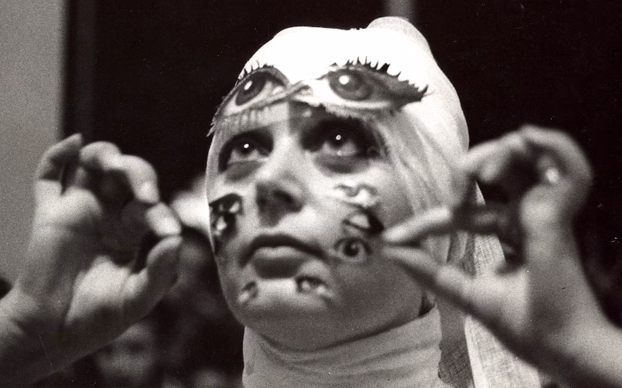 Primo piano del volto dell'artista Tomaso Binga mentre si incolla sul viso ritagli di immagini di occhi.